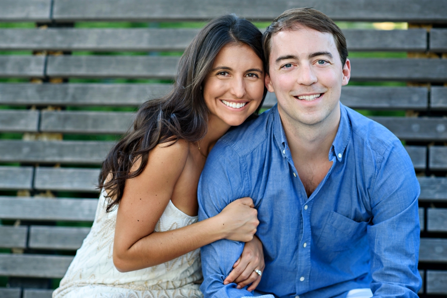 A woman holds onto her husband to be's arm and smiles in their battery park engagement session.